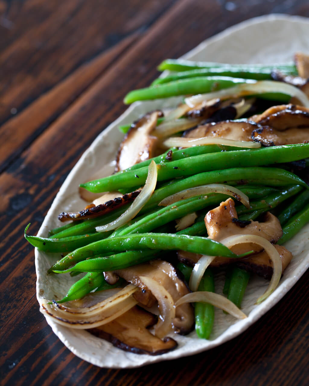 A plate of green beans and mushrooms on top of a table.