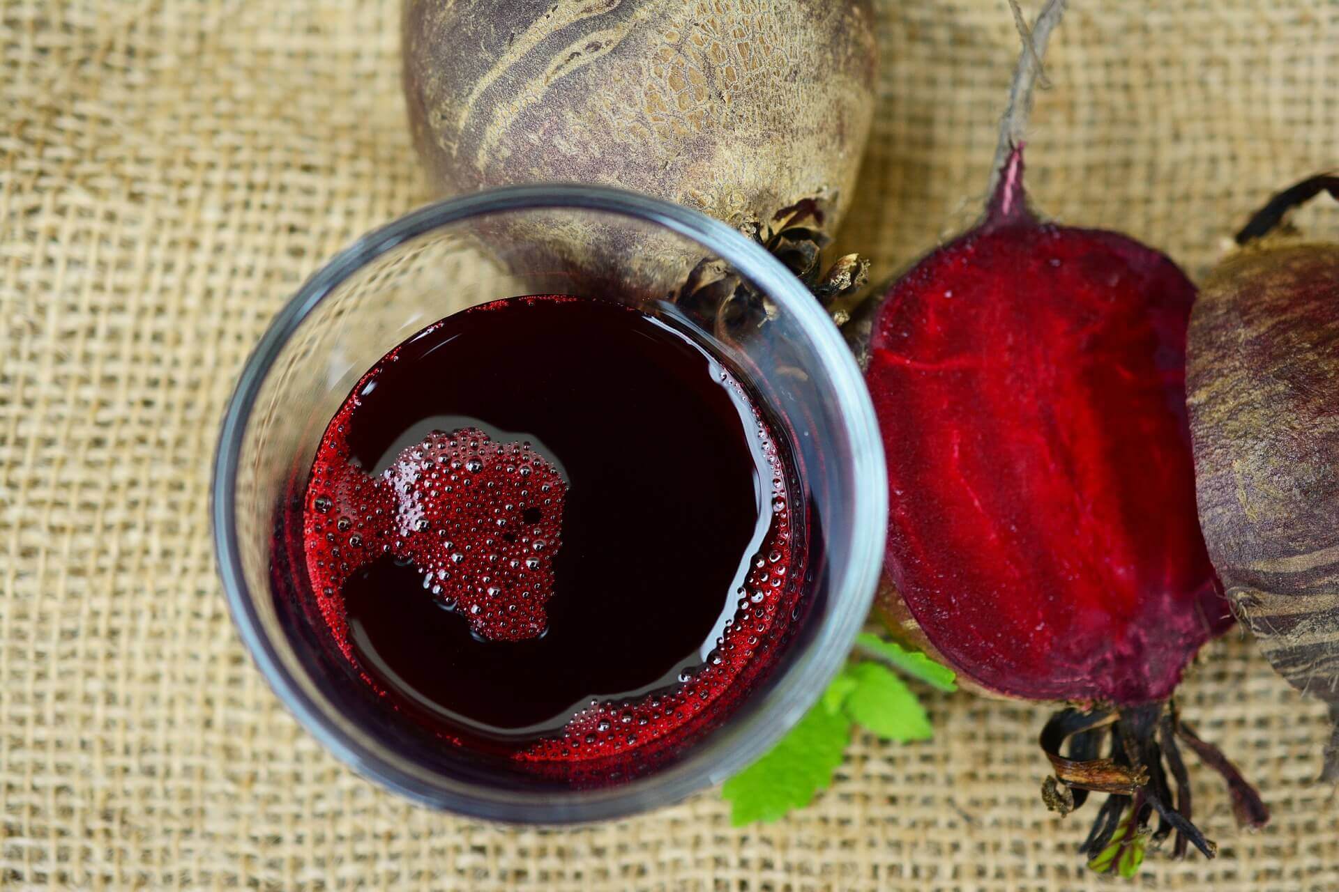 A glass of red liquid next to some beets.