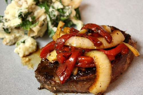 A steak with peppers and onions on top of it.